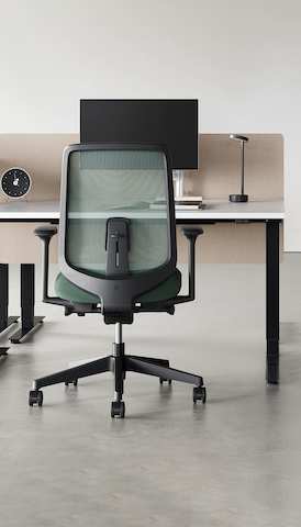 A black Verus Chair with dark green suspension back pulled up to a black Nevi Sit-Stand Desk with a Civic Table and Portrait Chair in the background.