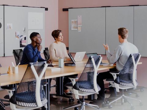 People meeting at seated-height tables with project work pinned on boards attached to the wall.