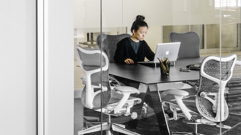 A professional working on a computer while seated at a Mirra 2 chair around a meeting table.