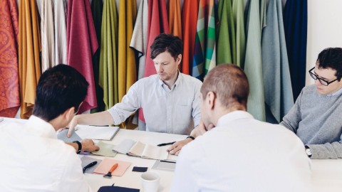 Four businessmen around a table examine various brightly colored fabric swatches.