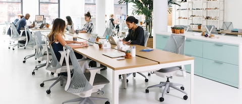 A handful of colleagues work independently in an open office that features a benching setup with light grey Sayl office chairs. A handful of colleagues work independently in an open office that features a benching setup with light grey Sayl office chairs.