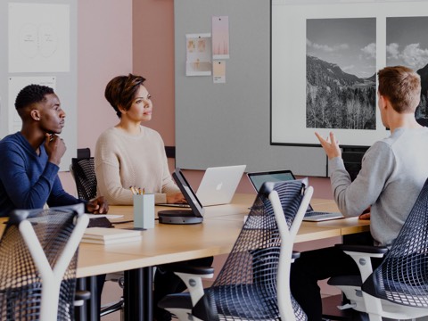 Photo of three people sitting around a laptop and discussing workplace strategy. They are sitting in blue Sayl Chairs. 