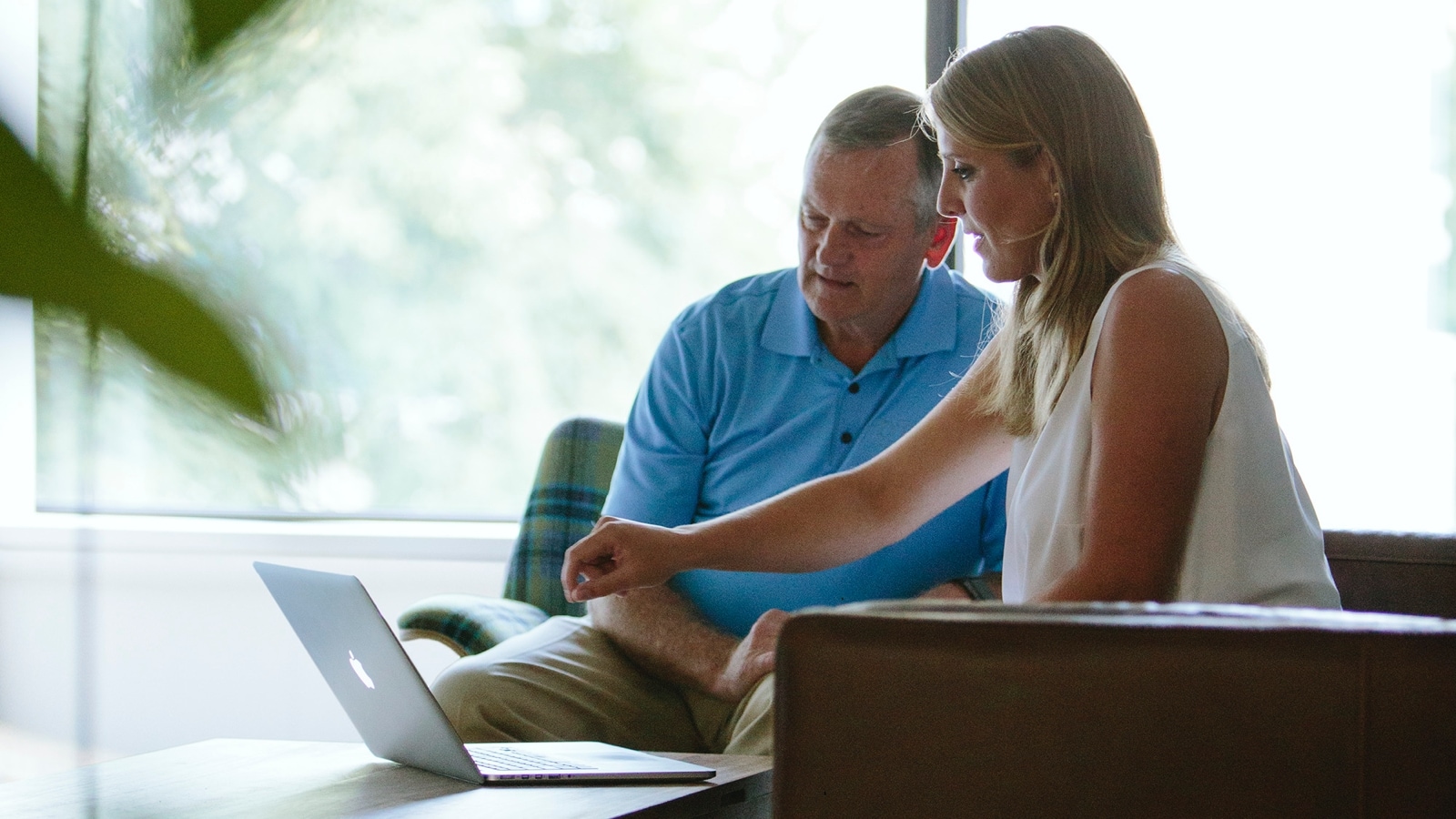 Two people sitting in lounge seating discussing work that's being displayed on a laptop.