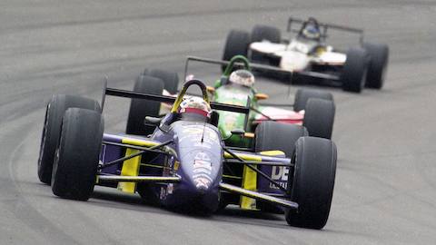 Three Indy cars turn the corner of a racetrack.