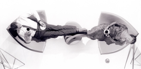 A man and a woman relaxing in a pair of Nelson Coconut Lounge Chairs while sharing an ottoman. 