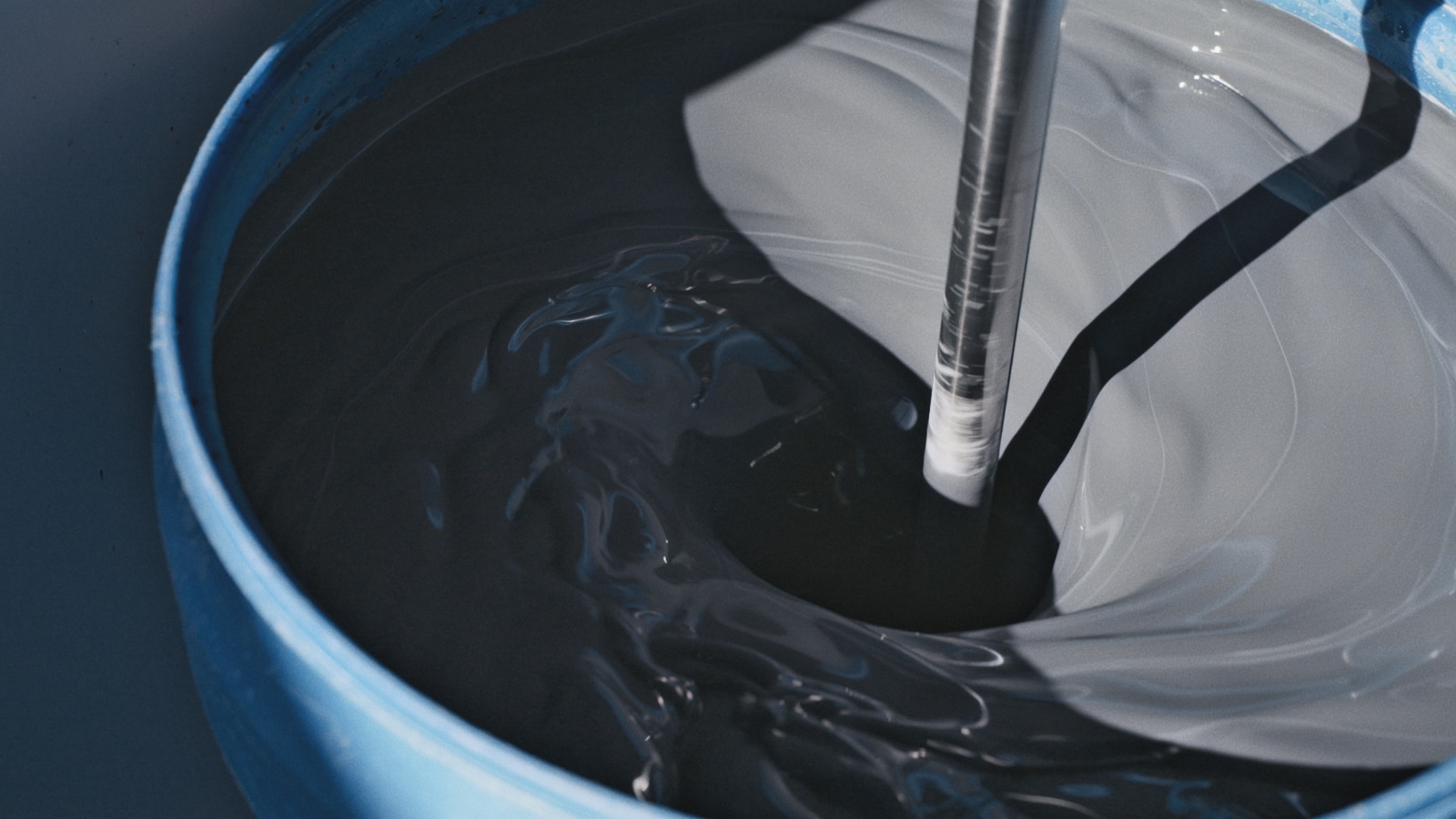 A blue blunger, or large stand mixer, with dark gray slurry (clay and water combined).