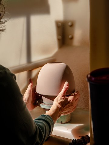 A set of hands placing an unglazed clay bowl into the glazing booth.