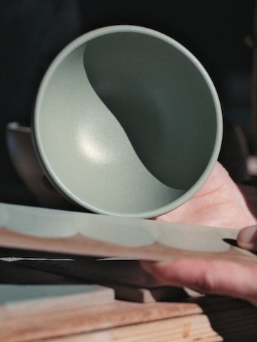 A pair of hands holds a finished bowl against a reference piece for color matching.
