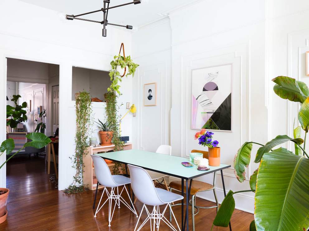 A residential dining area featuring a rectangular table, white Eames Molded Plastic Chairs, modern artwork, and plants. A residential dining area featuring a rectangular table, white Eames Molded Plastic Chairs, modern artwork, and plants.