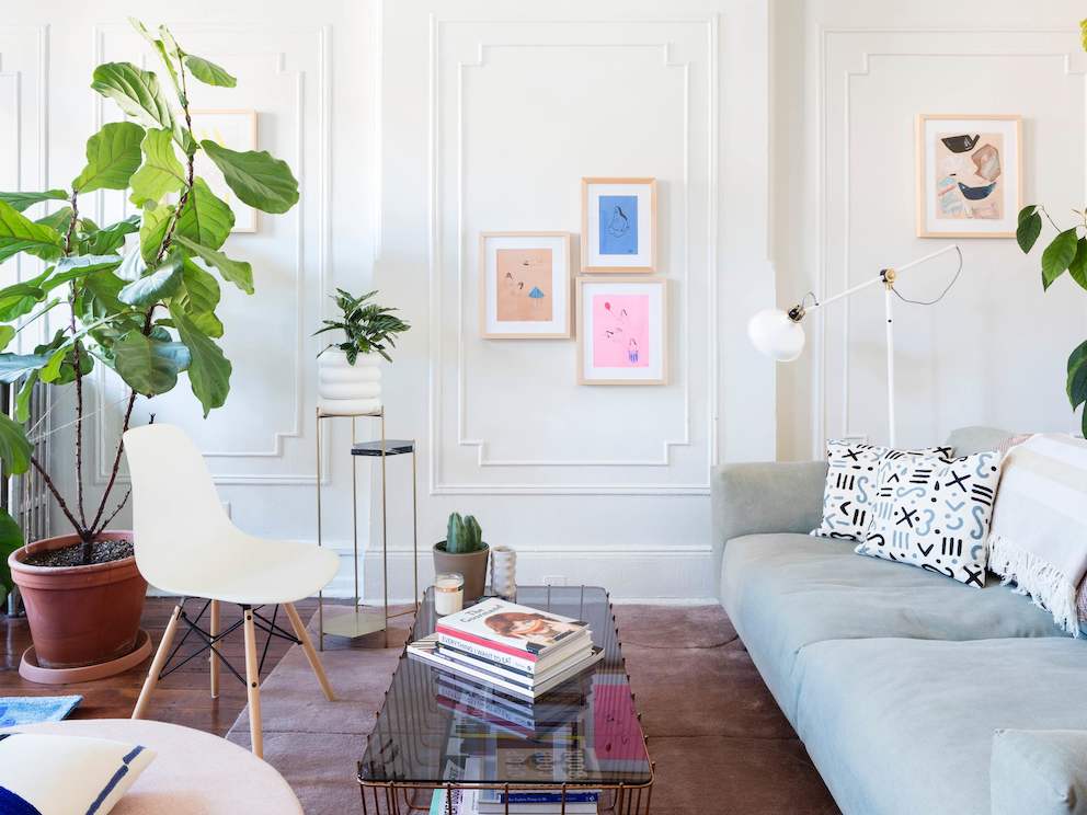 A living area featuring a gray sofa, a glass-top coffee table, and a white Eames Molded Plastic Chair with dowel legs.