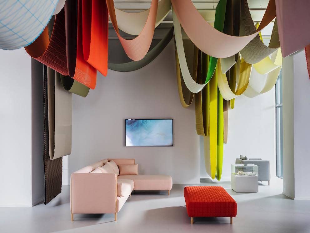 A pink ColourForm sectional and a red ColourForm ottoman beneath hanging textiles of various colors.