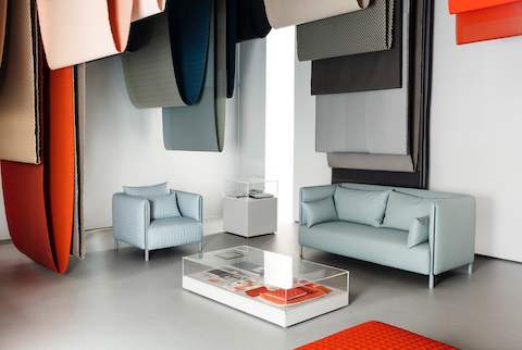 Blue ColourForm seating beneath hanging textiles of various colours.