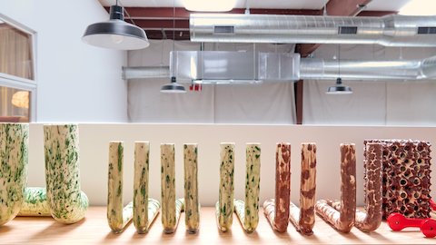 A set of tubular speckled white and green ceramic pieces and speckled brown and white ceramic pieces sit atop a wood table.