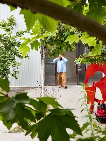 Benjamin Critton outside of Marta gallery, framed by a tree and red metal sculpture.