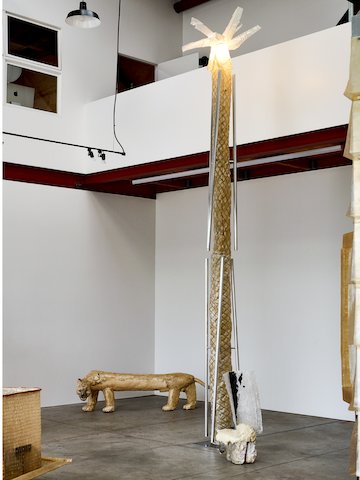 Phantom-22, an exhibition by Minjae Kim featuring a plaster mountain lion and quilted fiberglass palm tree, is on display in the gallery space with cement floors and white walls.
