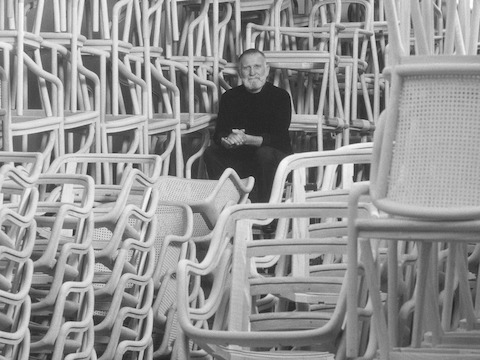 Designer Ward Bennett sits among dozens of stacked chairs.