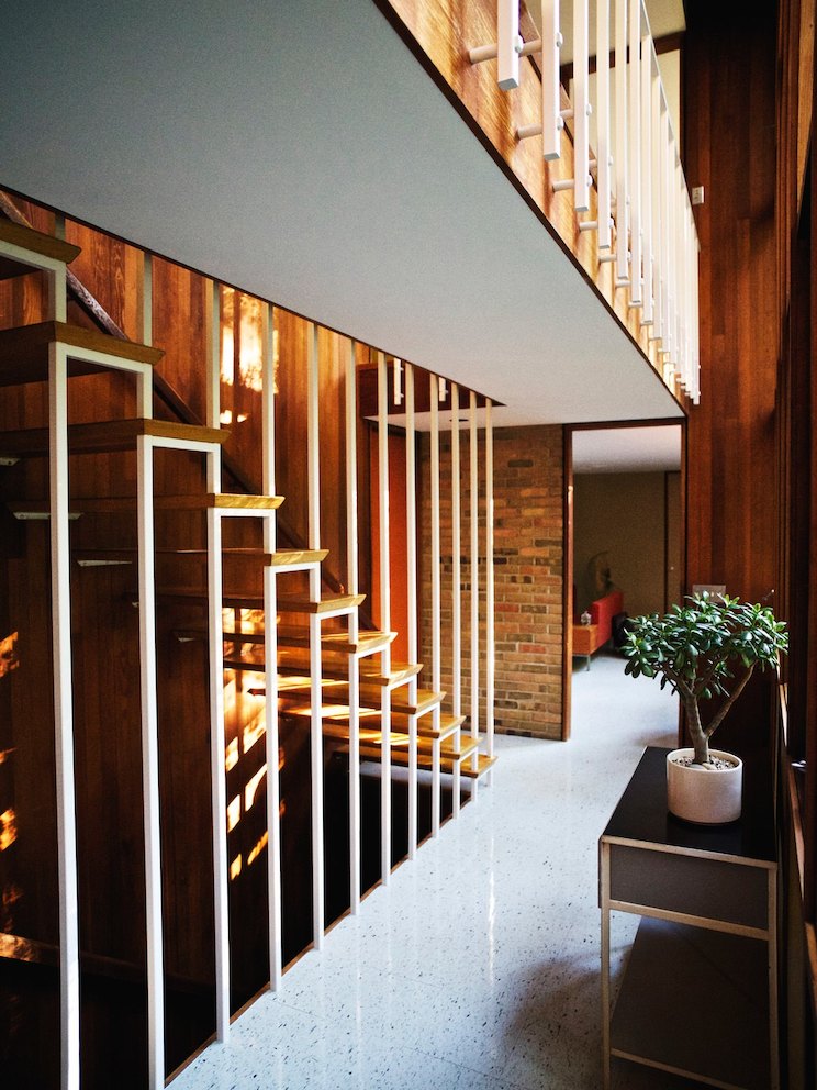 A staircase with treads cantilevered from the redwood wall and suspended by a bank of ceiling-height balusters. 