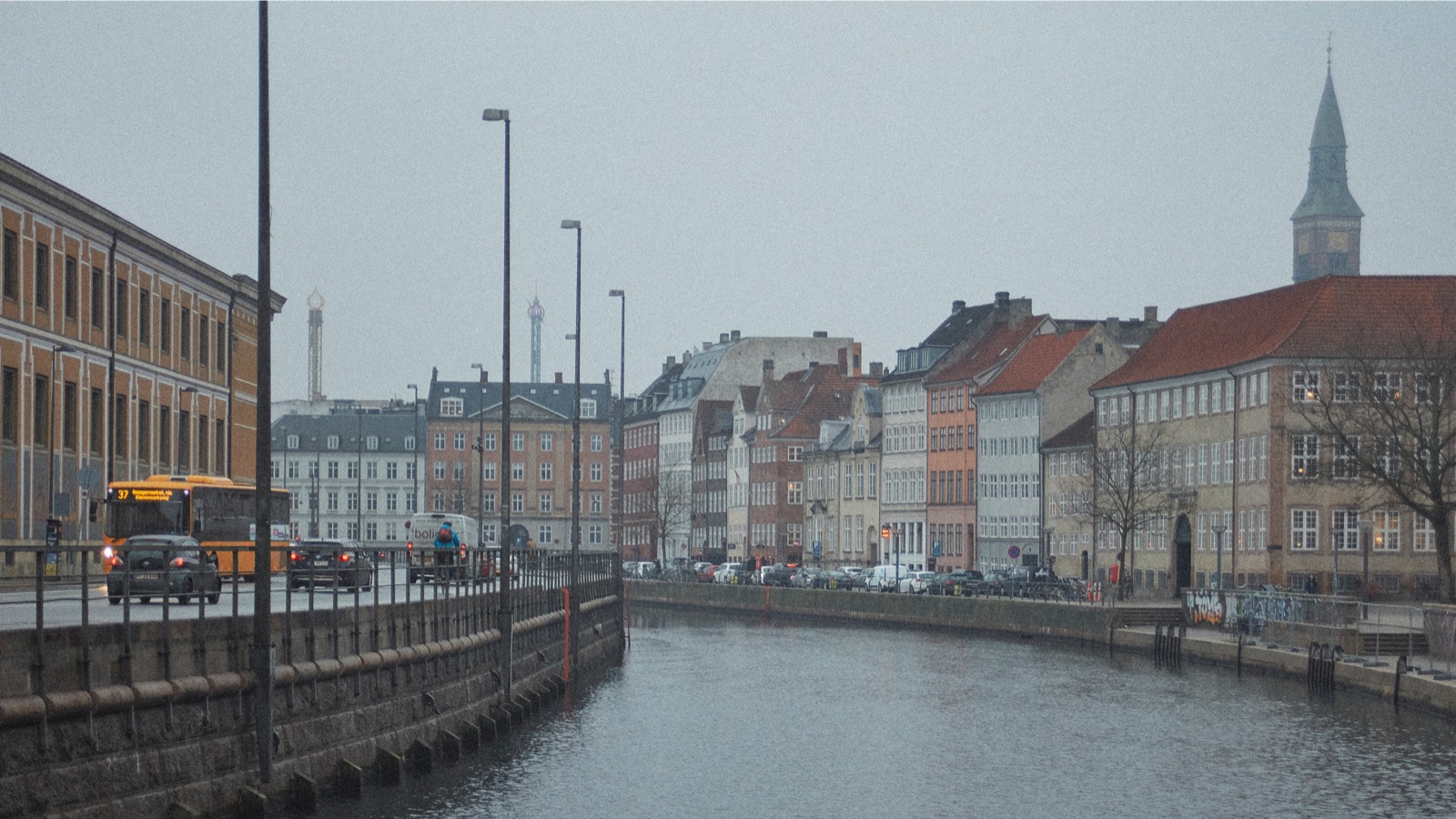 A river on a rainy day in Copenhagen, with buildings on the right and a road on the left.