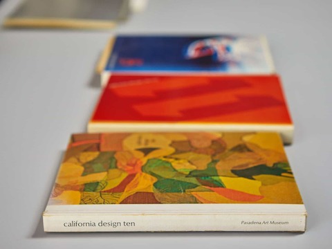 Three colorful books laid out on a white surface; the book in focus is called 'california design ten' from the Pasadena Art Museum.