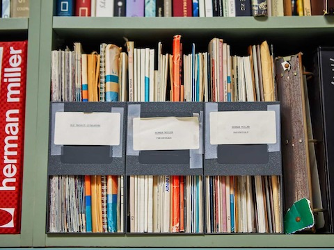 Closeup of Don Chadwick's full bookshelf, which features various Herman Miller books, a catalog, and product literature.