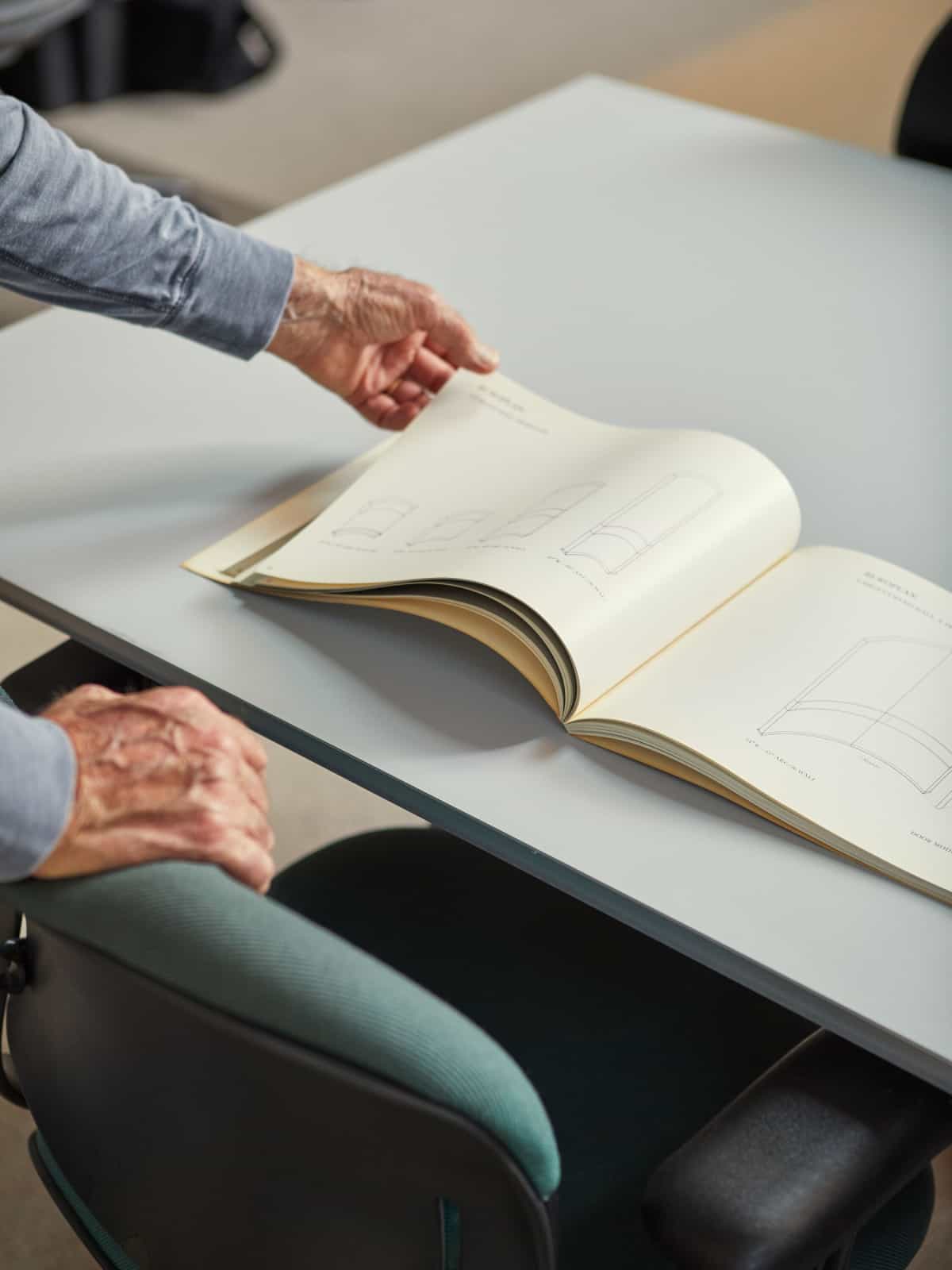 Don Chadwick flips through a book sitting on a gray conference table.