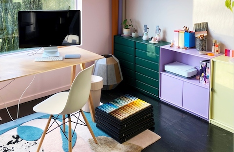 The home office of artist/designer Alex Proba includes a simple desk and chair with a view of nature, and colorful storage units along a wall.