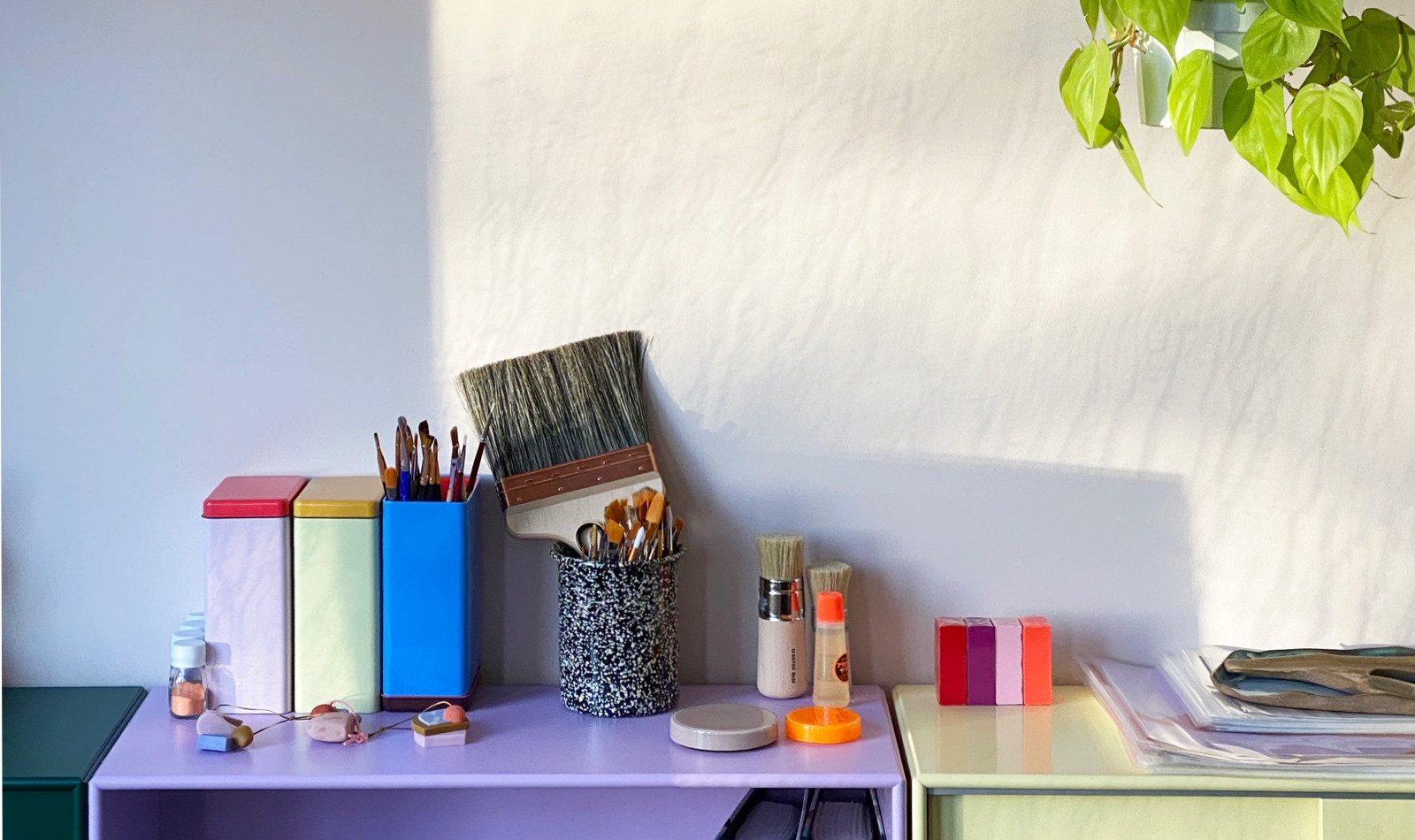 Natural light streams over paint brushes and other artist tools neatly arranged atop colorful storage cabinets in the home studio of artist/designer Alex Proba.