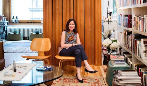 A portrait of designer Ayse Birsel, sitting in an Eames Molded Plywood Lounge Chair next to an Eames Molded Plywood Folding Screen, in her home studio in New York City.