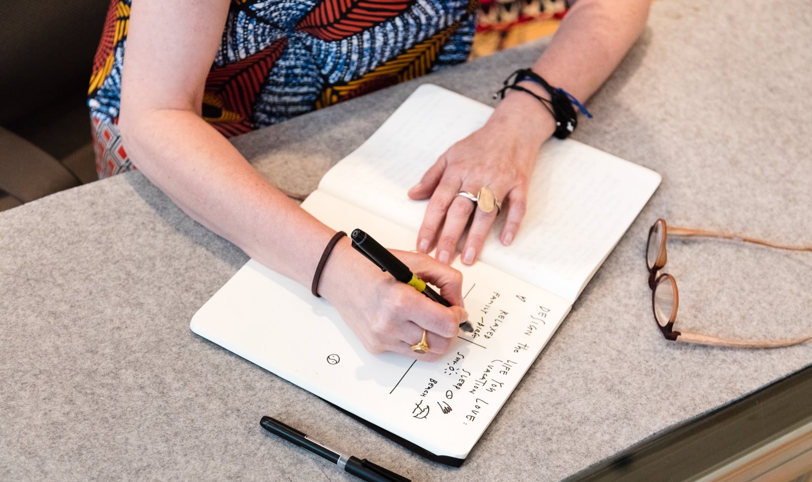 An overhead shot of Ayse Birsel drawing in her notebook with an extra pen and a pair of glasses on the table.