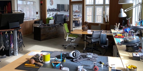 Designer Brian Alexander's home studio with a large desk, tools, parts for his designs, a laptop and monitor, and a green Embody Chair.