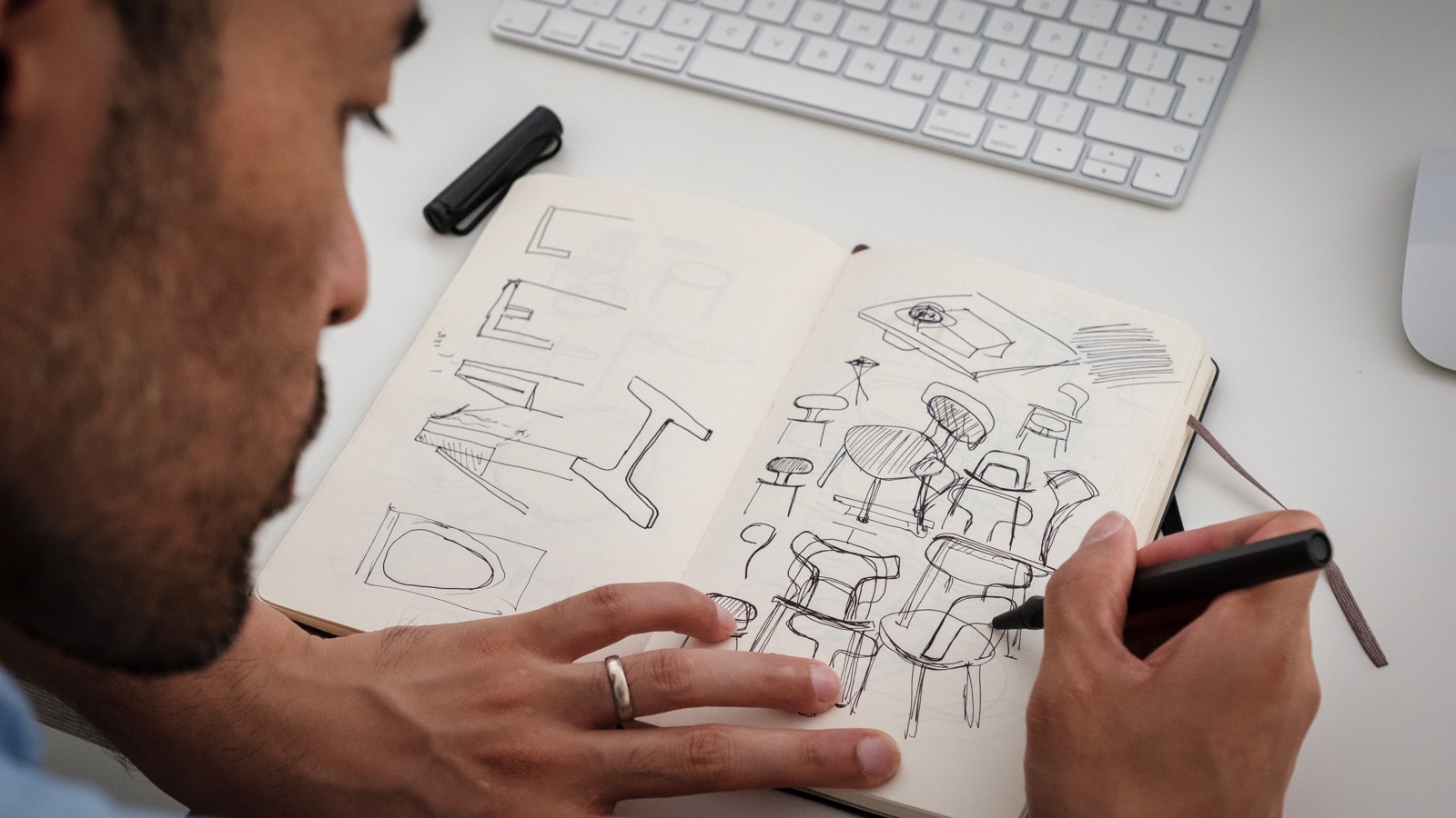 Japanese-born designer Keiji Takeuchi sits at the desk in his home studio in Milan, Italy and sketches ideas for a chair design in a notebook.