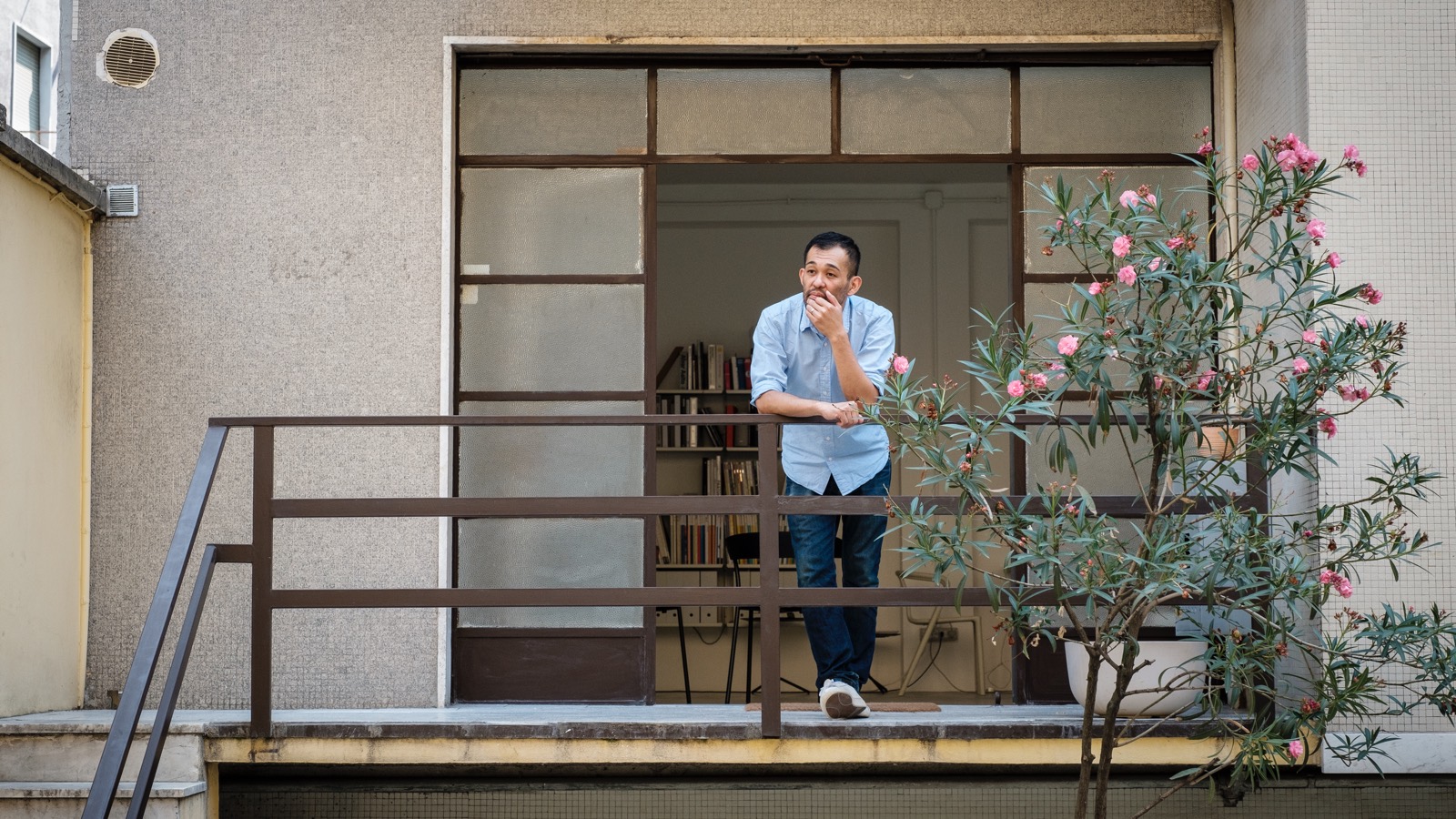 イタリアのミラノのホームスタジオの外で、花を付けた木の横で佇むデザイナー、ケイジ・タケウチ