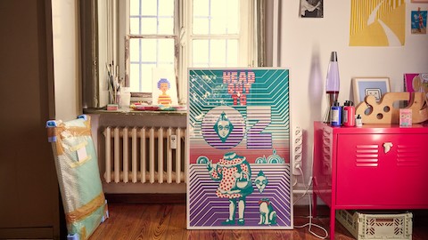 Olimpia Zagnoli's artwork propped against a wall in her studio, alongside a red metal cabinet holding art supplies.