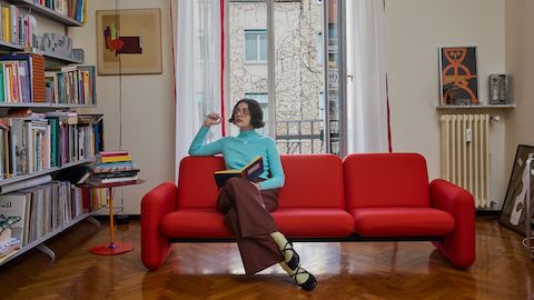 Illustrator Olimpia Zagnoli on a red chiclet sofa from Herman Miller in front of a large window in her home.