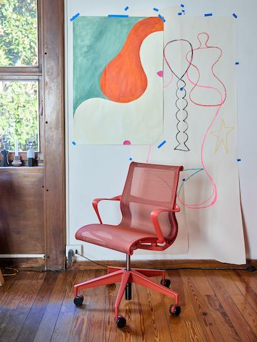 An empty red Setu chair by Herman Miller in front of a wall displaying artistic sketches in Olimpia Zagnoli's studio.