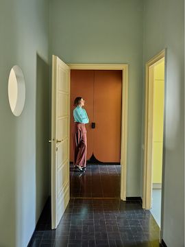 Olimpia Zagnoli standing in her home at the end of a hallway, just beyond an open door.
