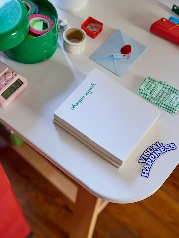 Desk with note paper labelled Olimpia Zagnoli and various office supplies and a sticker reading Visual Happiness.