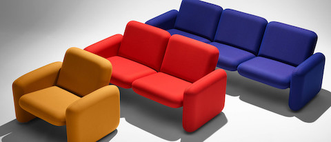 A yellow Wilkes Modular Sofa Group Chair, a red Wilkes Modular 2 Seat Sofa and a blue Wilkes Modular 3 Seat Sofa each placed in front of each other angled in a line.