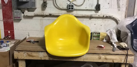 The yellow shell of an Eames-designed chair sits on a workbench.