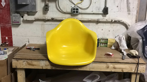 De gele schaal van een stoel ontworpen door Eames zit op een werkbank. Selecteer om naar een artikel over de geschiedenis van Eames Shell-stoelen te gaan.