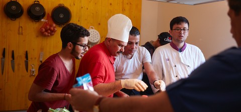 Four men interact while preparing food.