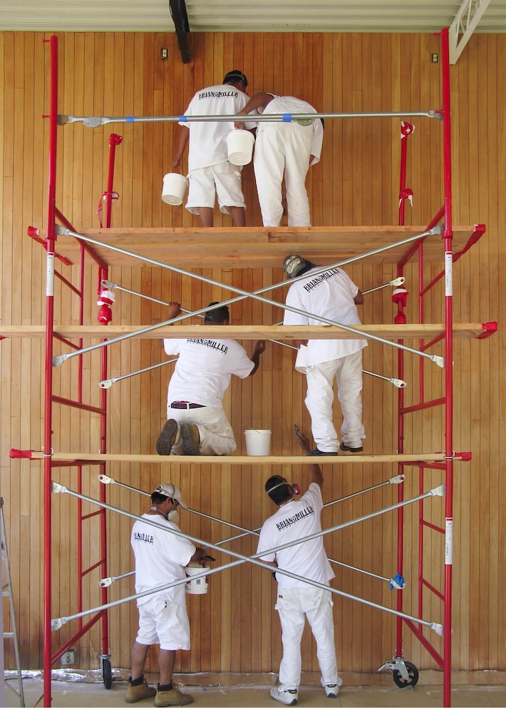 彩色照片里有六个男人在红色的脚手架上工作，修理Eames House起居室的墙壁。 