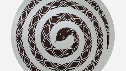 Vista aérea de una mesa redonda y ocasional con la imagen de una serpiente enrollada. Seleccione para ir a un artículo sobre diseños inadaptados Herman Miller.