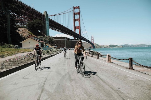 Three bicyclists pedal near the Golden Gate Bridge.