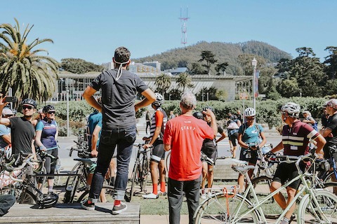 Dismounted bicyclists admire an architecturally distinct building in the distance.