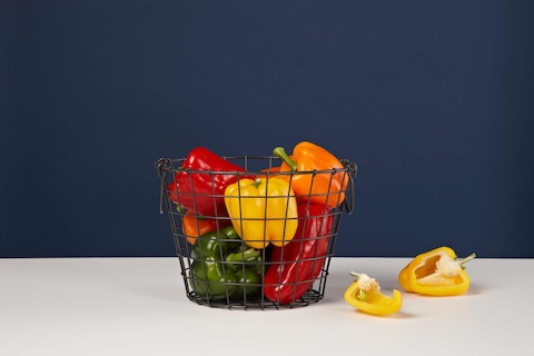 A black wire basket containing colorful peppers. A black wire basket containing colorful peppers.