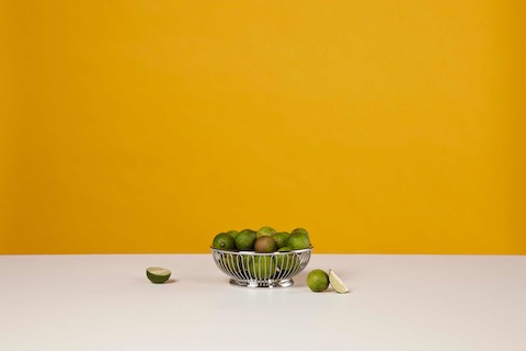 A small round wire basket containing limes.