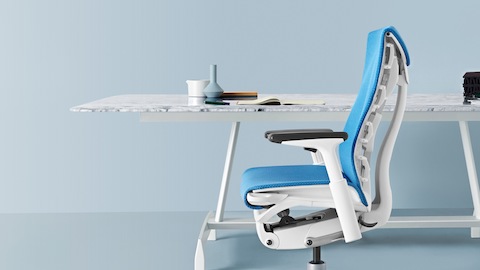 Side view of a blue Embody office chair at a white AGL Table.